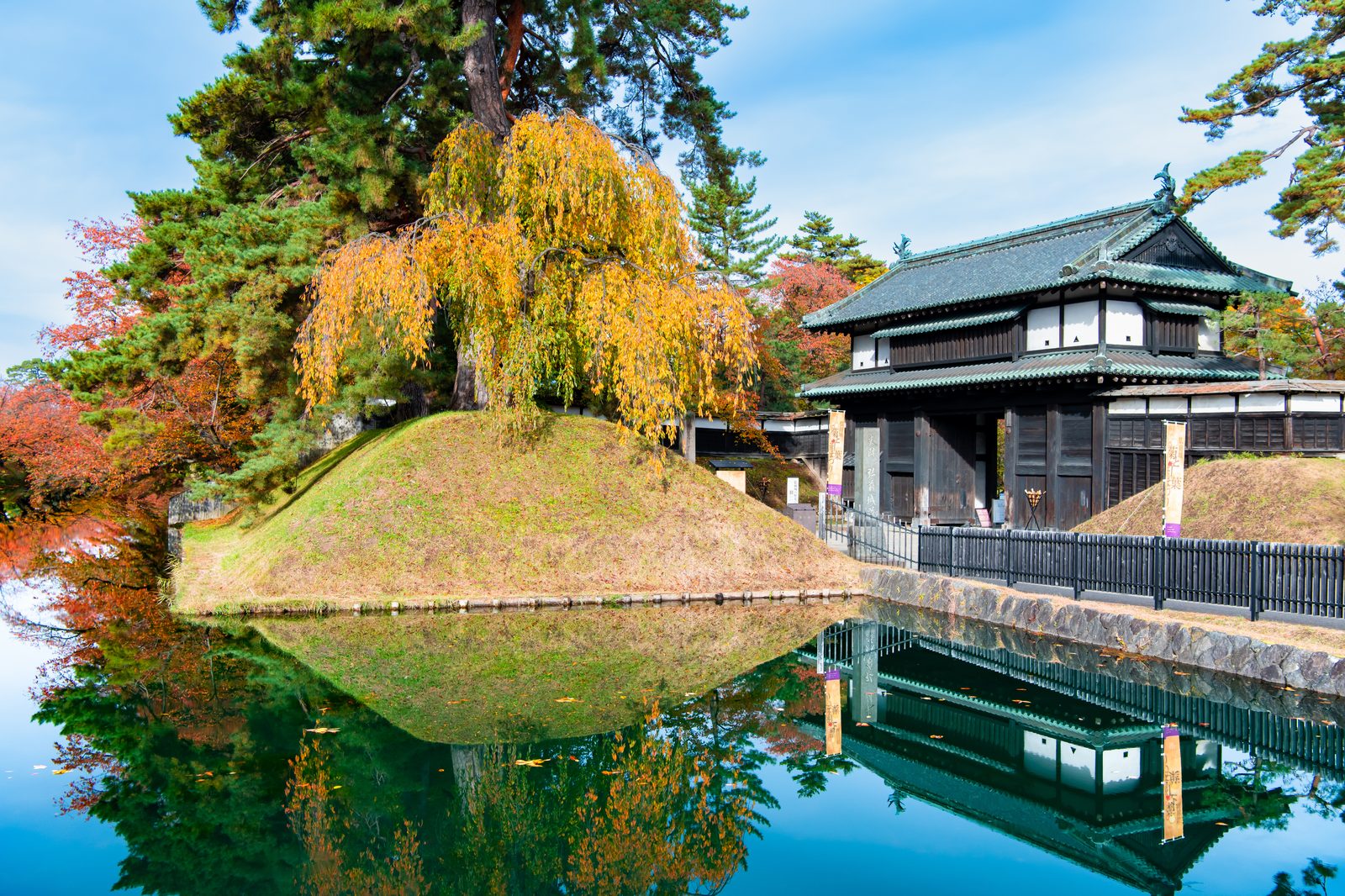 紅葉に囲まれた弘前城の追手門と、水面に映る城内の風景