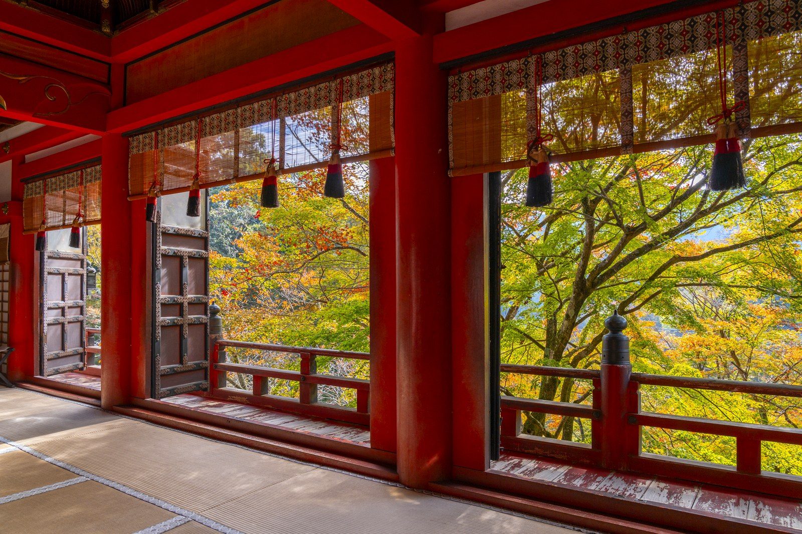 談山神社の拝殿の朱塗りの柱と簾ごしに見える黄葉した木々