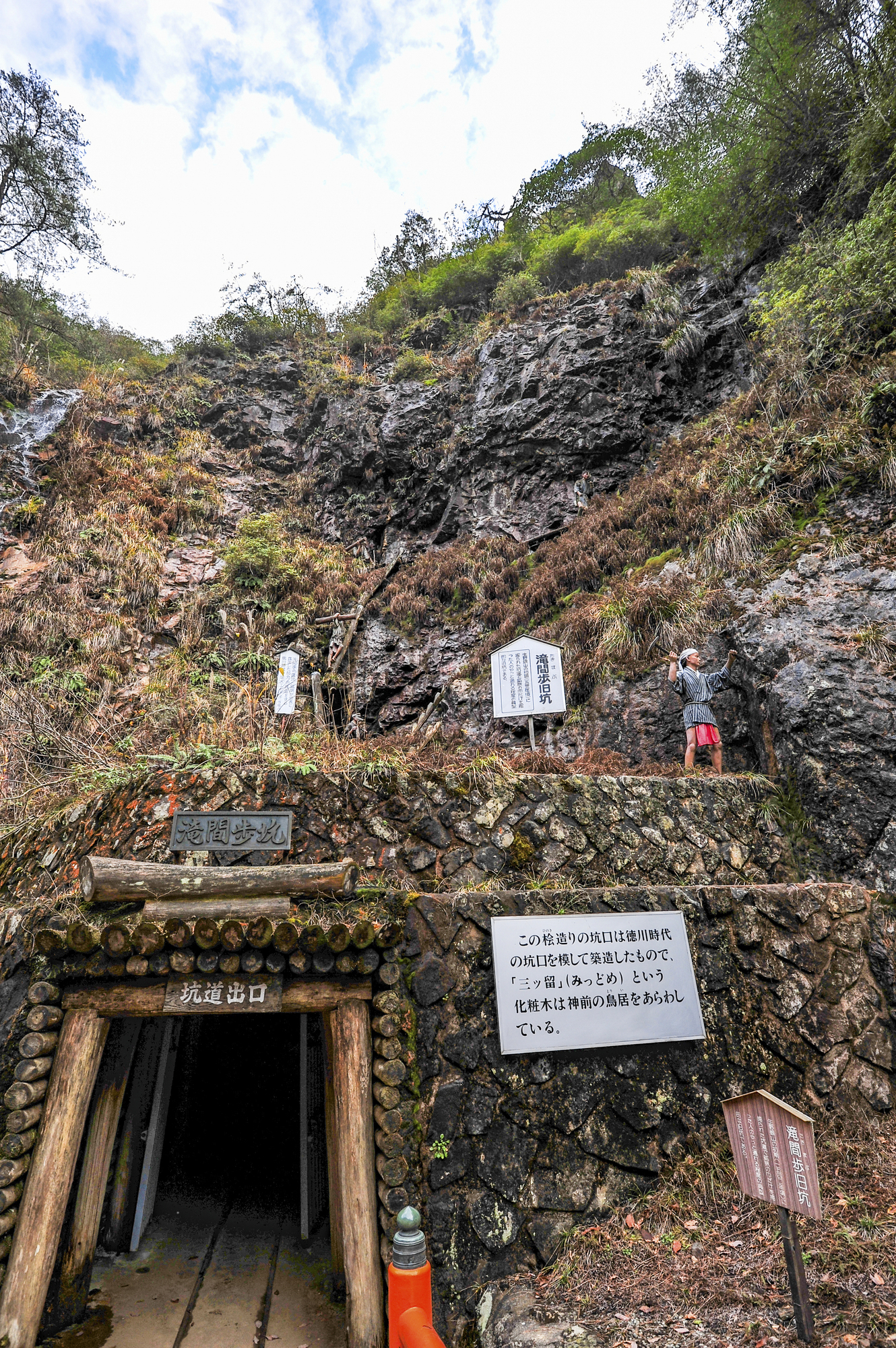 生野銀山の坑道出口。木組みの坑口の脇に説明看板が立ち、周囲は岩肌と草に覆われている