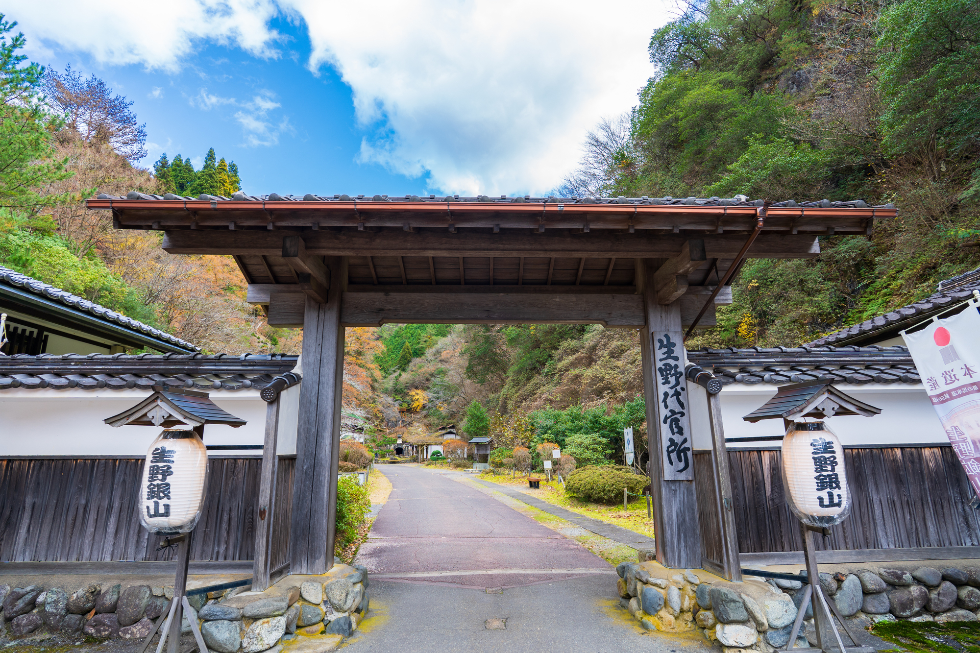 史跡生野銀山の入口の門。両側の門柱に「史跡生野銀山」と書かれた提灯が下がり、奥へ坂道が続いている