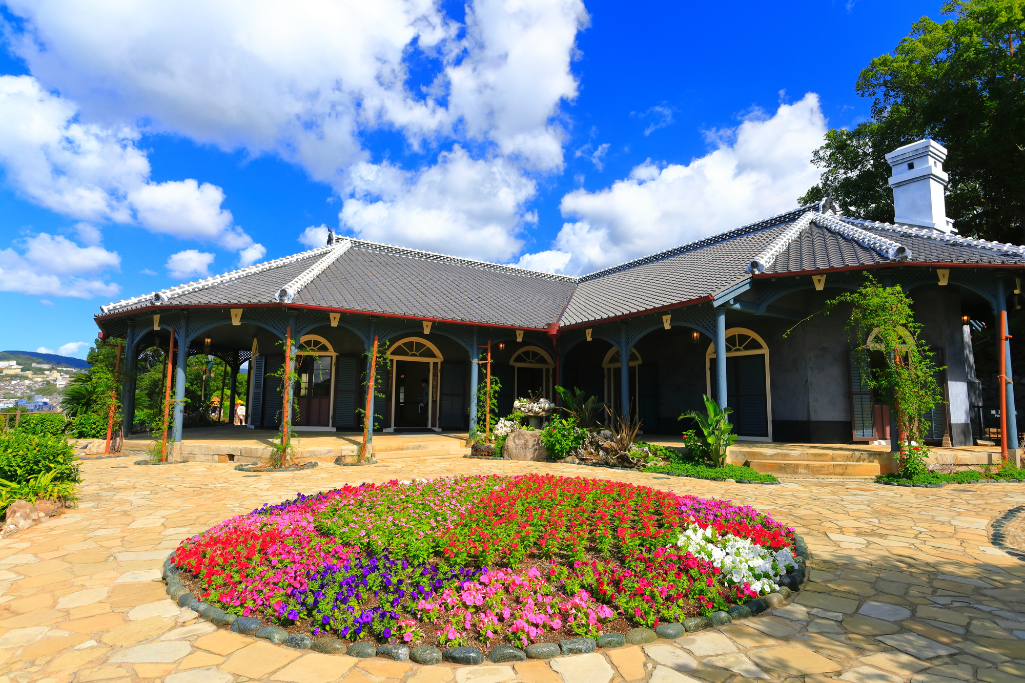 晴天のグラバー園に建つ旧グラバー住宅。前庭に花壇があり、建物の周囲をベランダが回っている